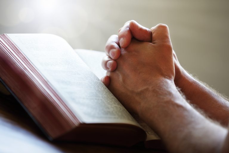 Hands folded in prayer on a Holy Bible