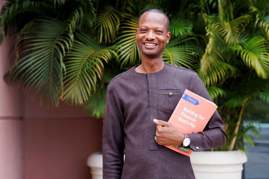 Young Ghana Businessman holding the Compass Biblical Financial Study Building Your Finances God's Way book.
