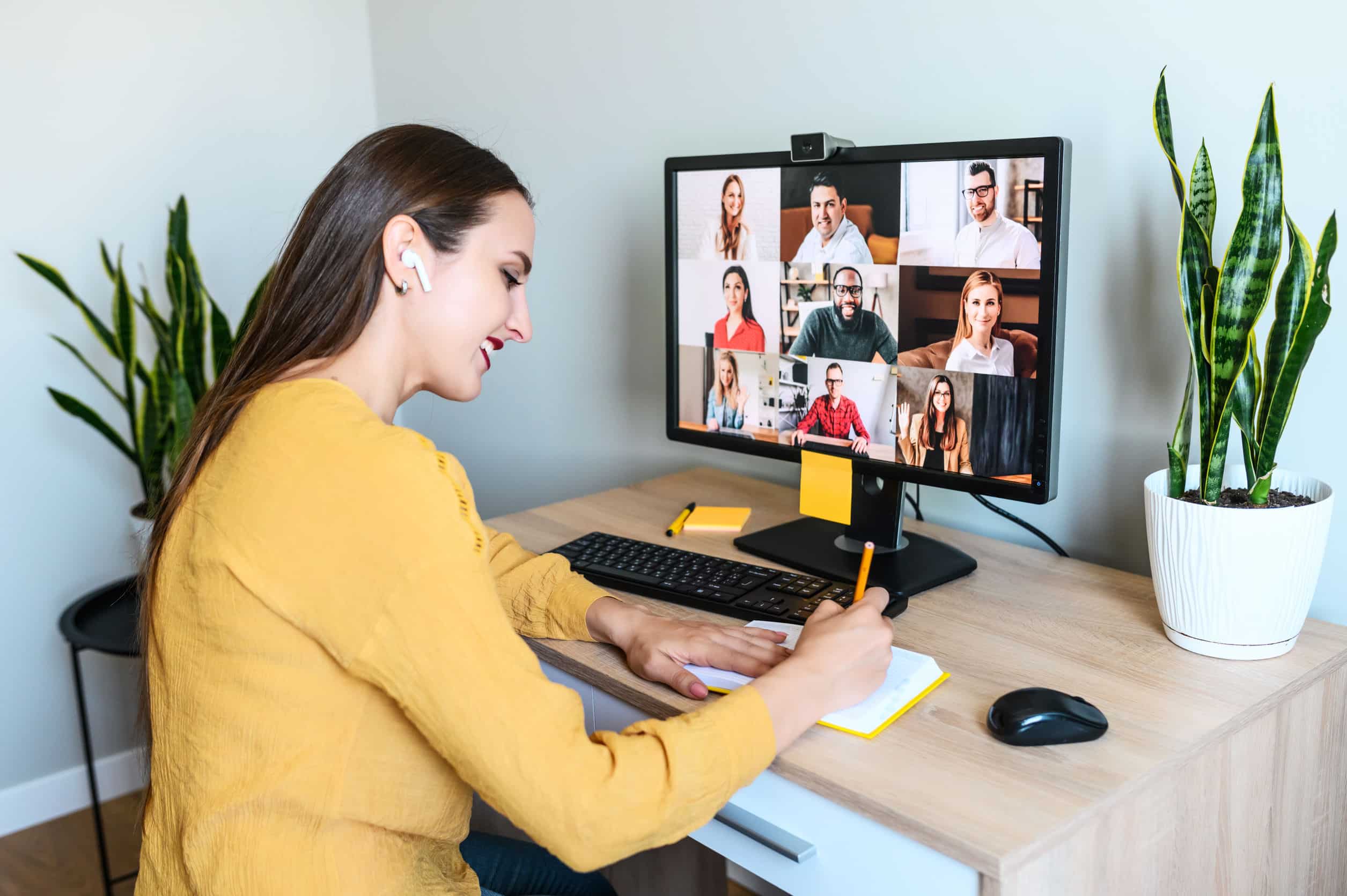 Woman sitting at a desk with a video call with 9 others on her computer.