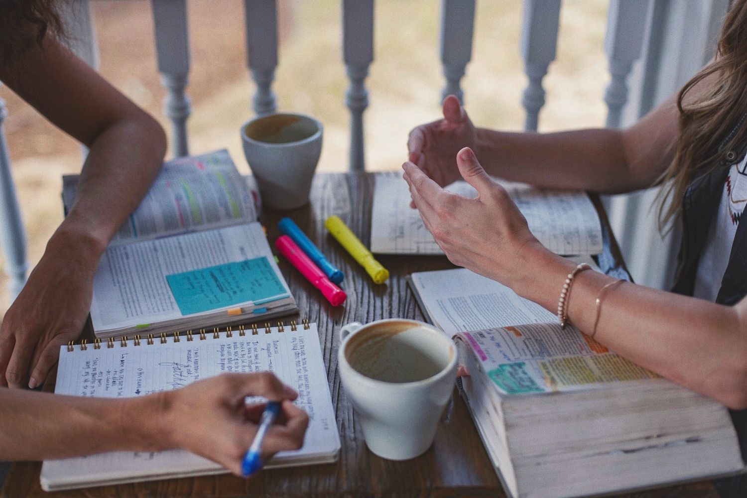Hands of two women with bibles, paper, pens and coffee on table. Join Compass to go deeper.
