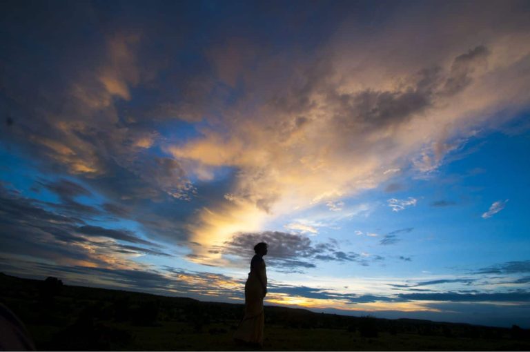 person standing alone during sunrise with clouds above